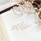 Open book with inspirational quote and dried flowers on a white surface