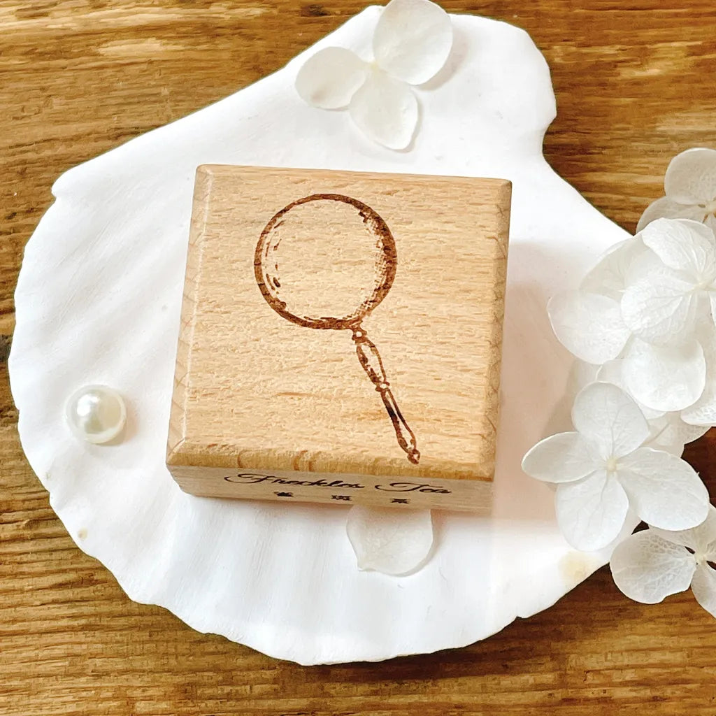 Wooden Magnifying Glass Rubber Stamp resting on a shell with flowers, styled close-up