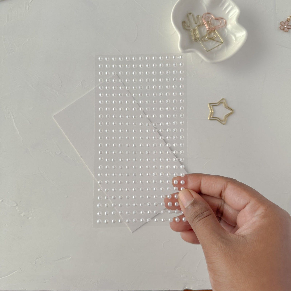 Hand holding a clear sheet of White Pearl Stickers Medium against a white background