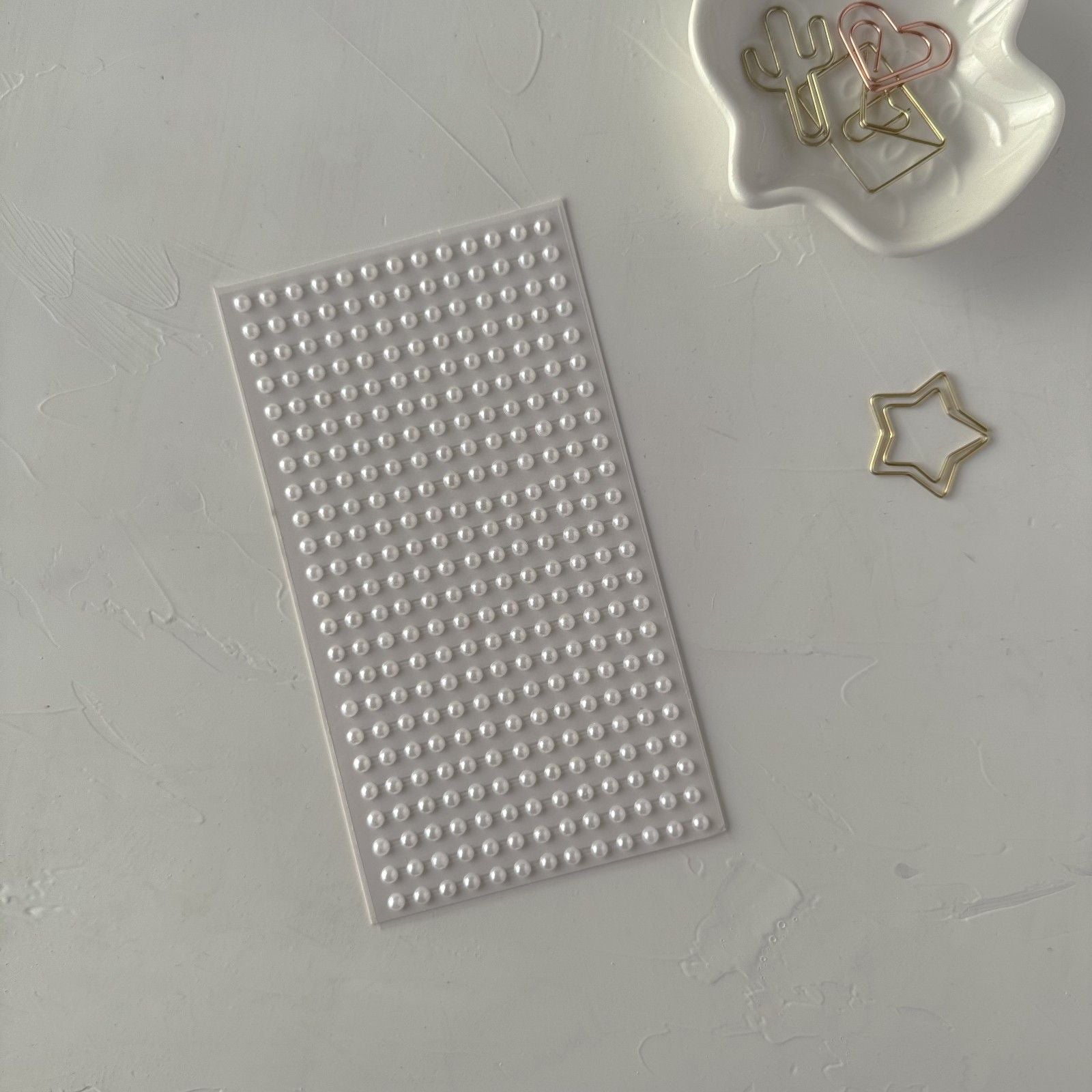 Sheet of small round stickers on a gray surface with decorative paper clips.