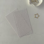Sheet of small round beads on a white surface with a star-shaped paper clip.
