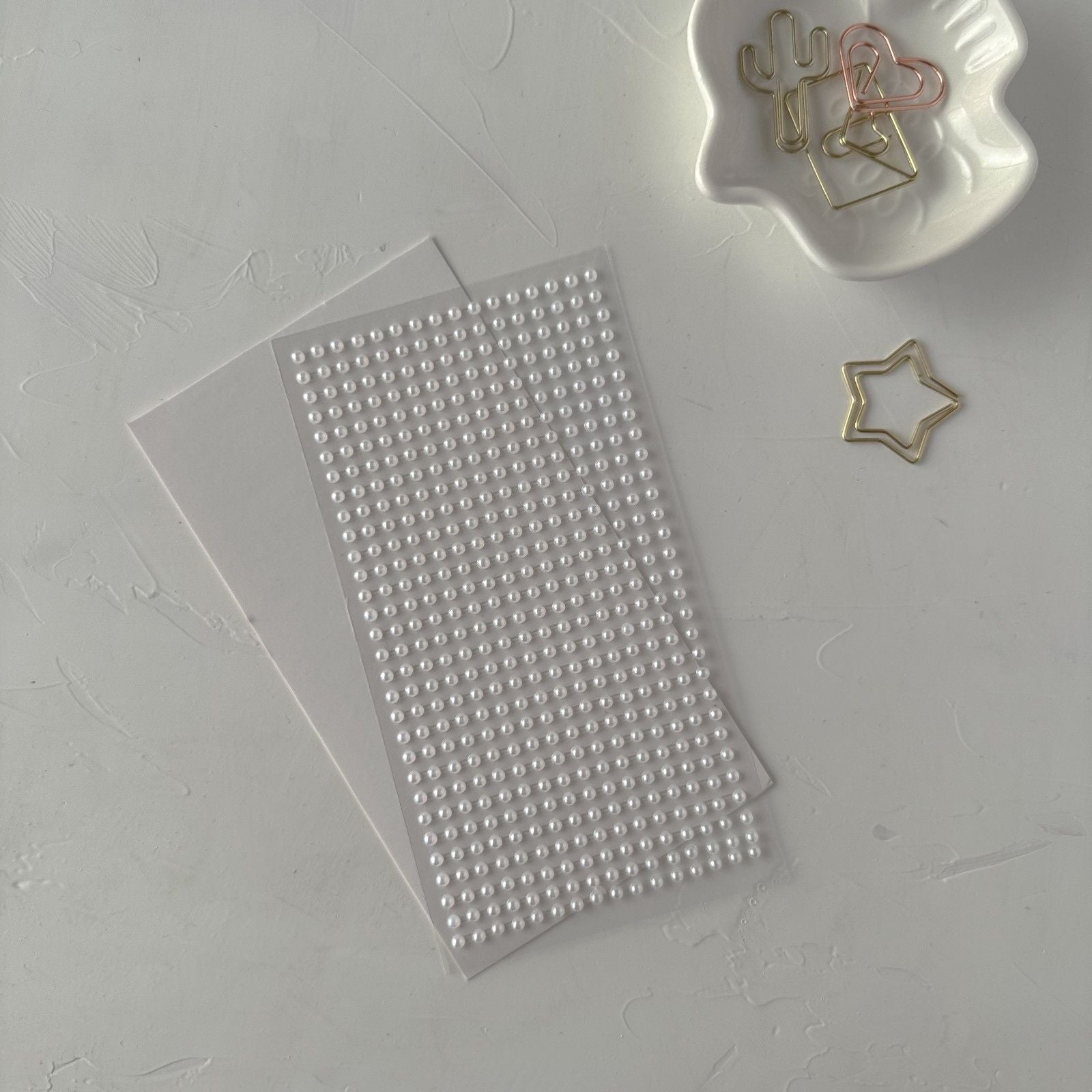 Sheet of small round stickers on a gray surface with decorative paper clips.