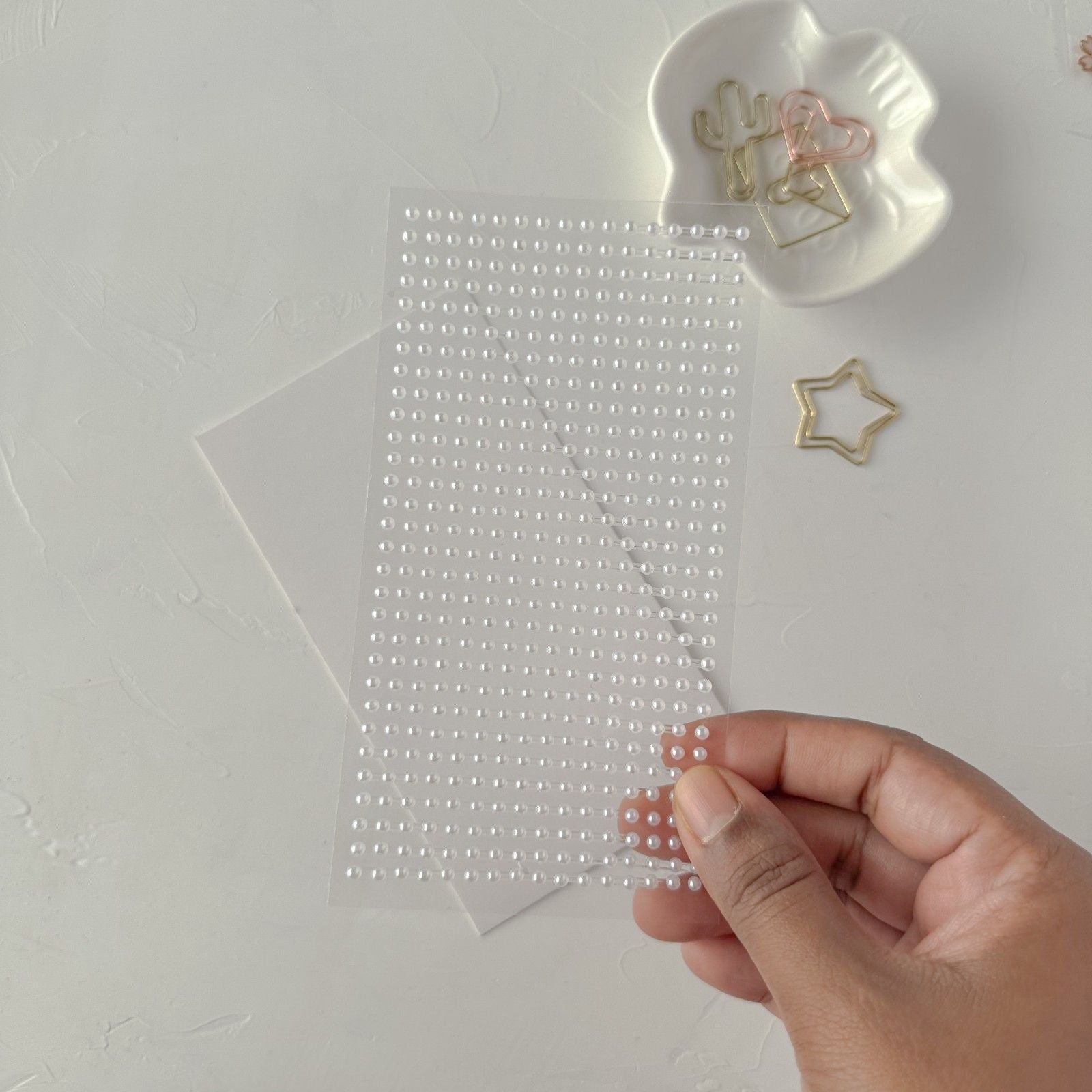 Hand holding a sheet of clear decorative stickers with a plain background
