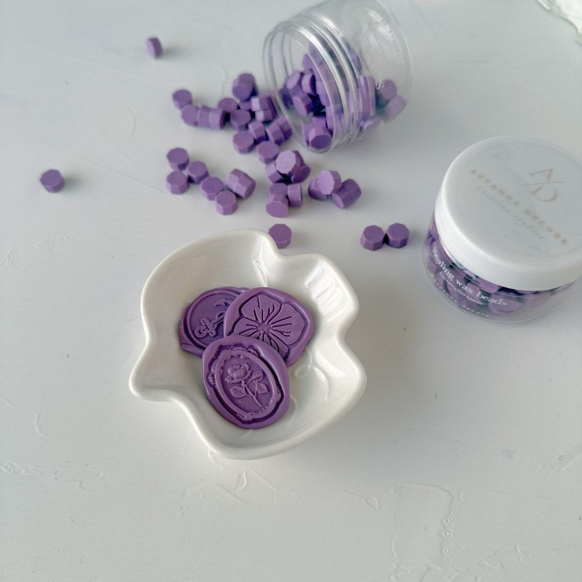 Round Wisteria Wax Beads in a soft floral lavender tone beside a white container on a light grey background