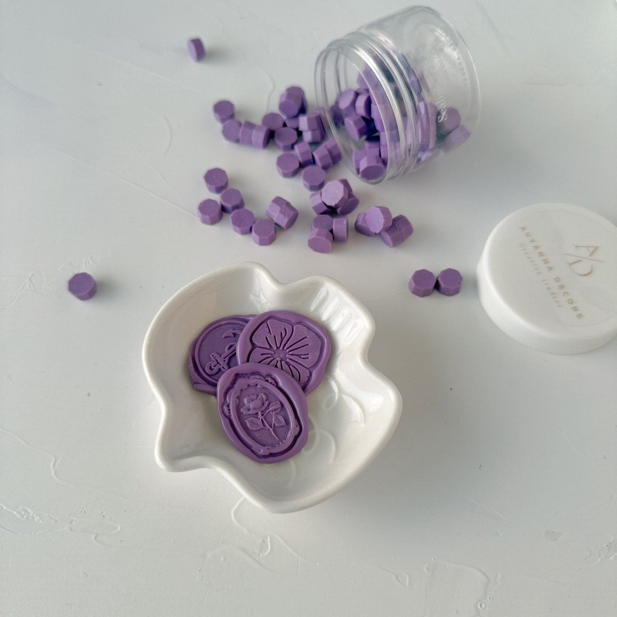 Hexagonal Wisteria Wax Beads in a gentle purple shade with a white dish on a light grey surface, top view