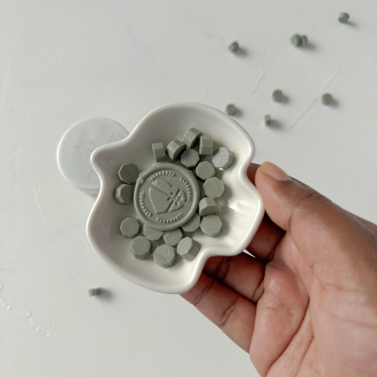Hand holding a ceramic mold of deep green Woodlands Wax Beads against a light grey studio background