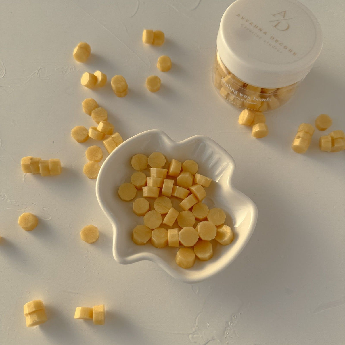 Sunny Yellow Marigold Wax Beads in a white dish beside the branded storage container on a grey backdrop