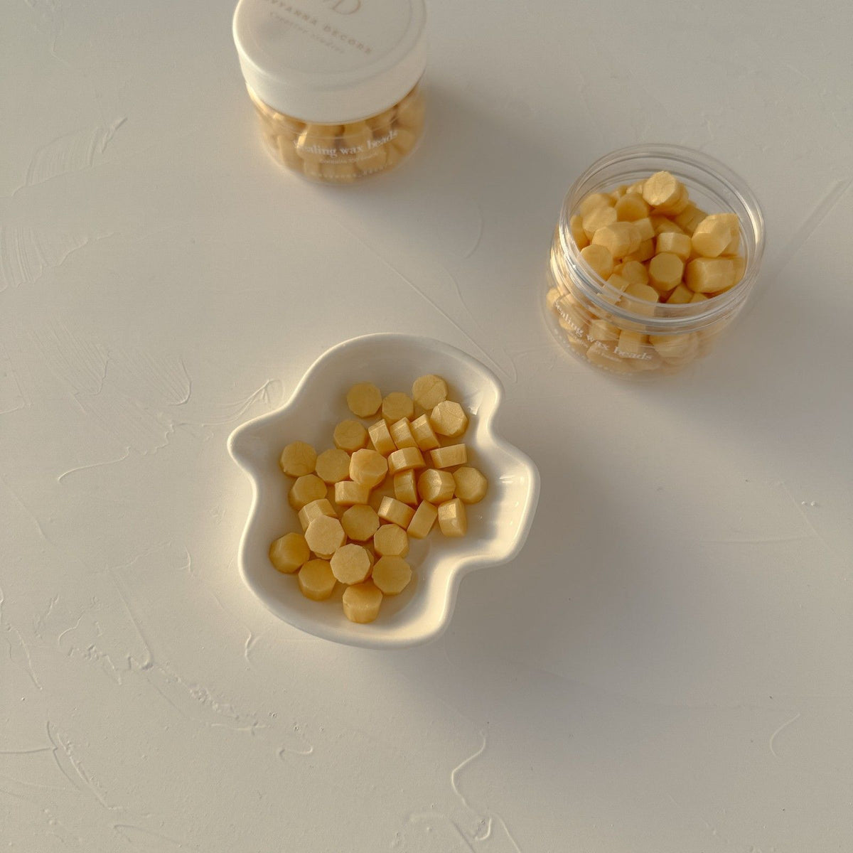 Yellow Marigold sealing wax beads filling a white bowl and clear container on a light grey surface