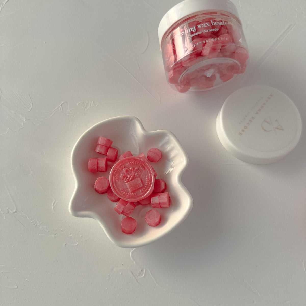 Young Wine wax beads in a white dish flanked by two storage containers on a light grey backdrop, top view