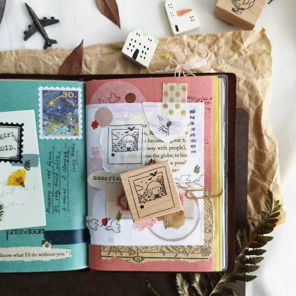 Open notebook decorated with Mini Girls Travel stamp prints on a clean white background