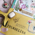 Decorative brooch on a 'Thumbelina' notebook with floral and nature-themed stationery items.