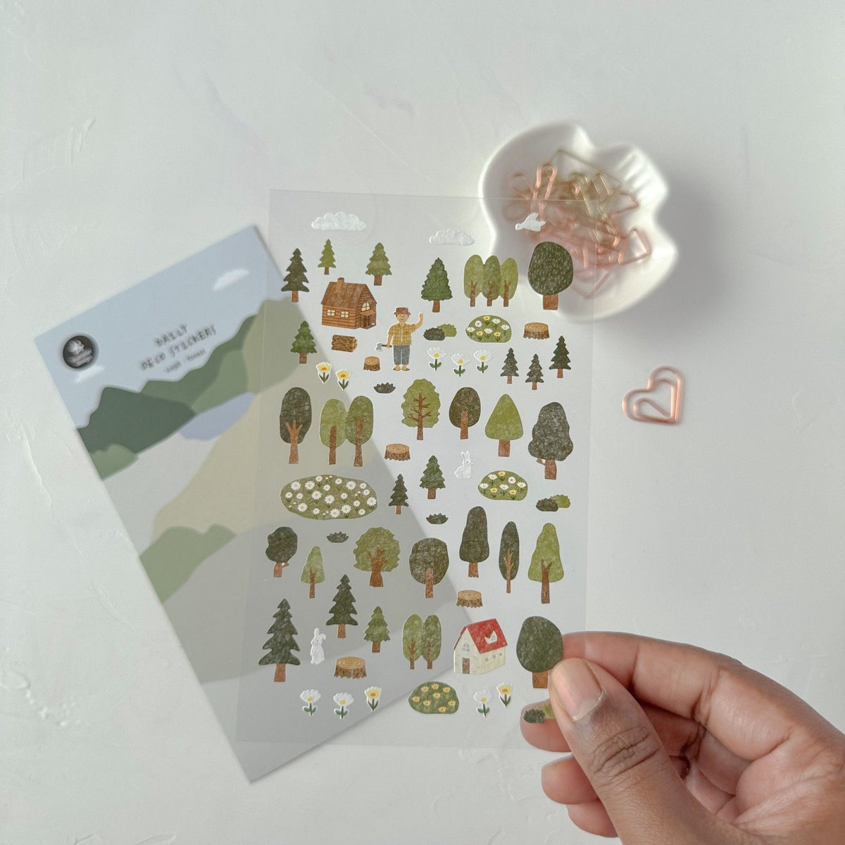 Pack of nature-themed stickers held by a hand on a light surface, from the Forest Sticker Sheet