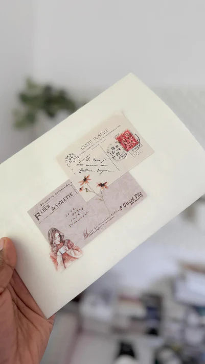 Hand holding a notebook with decorative postcard-style stickers on a blurred background