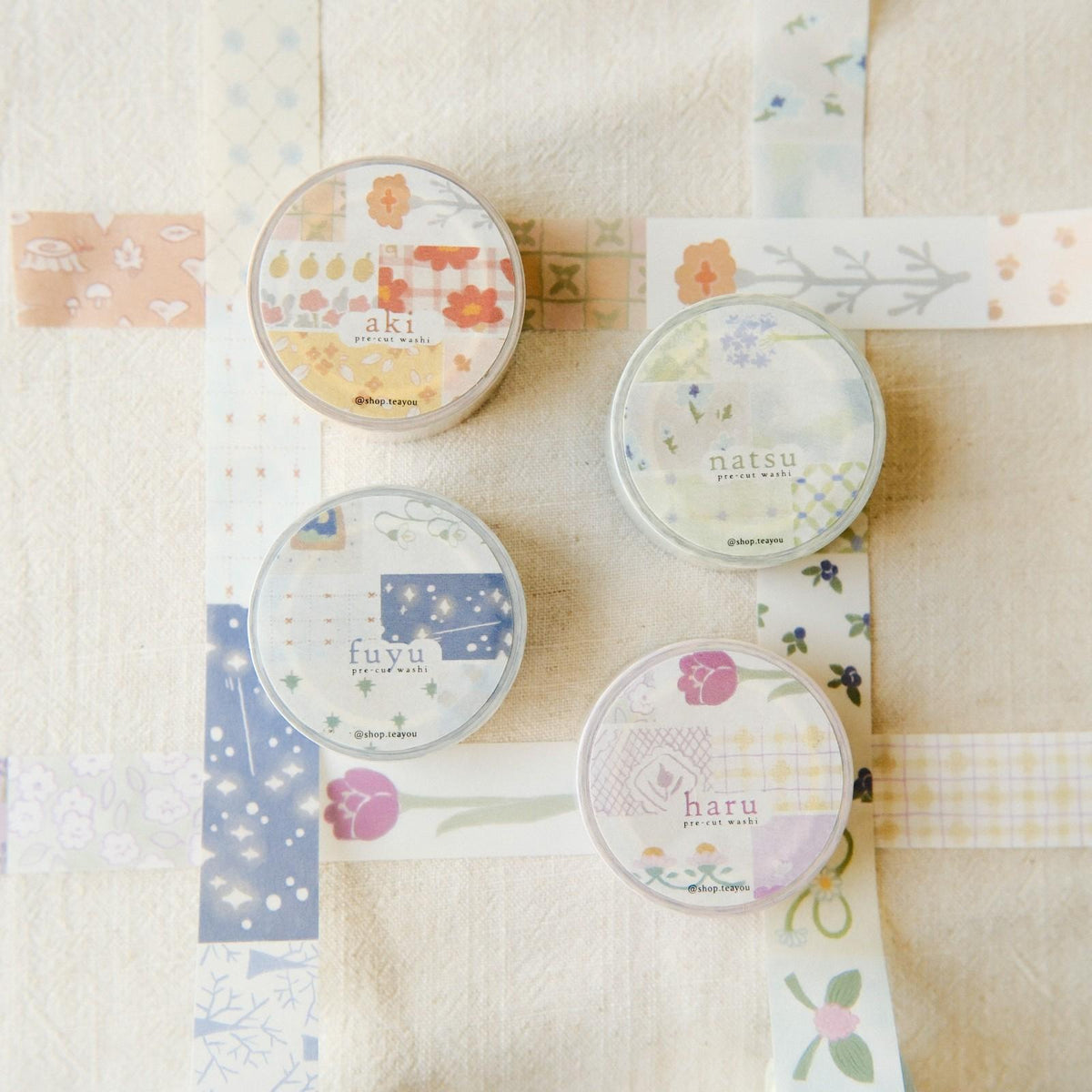 Four round containers labeled 'aki', 'natsu', 'fuyu', and 'haru' on a textured beige background with decorative paper strips.