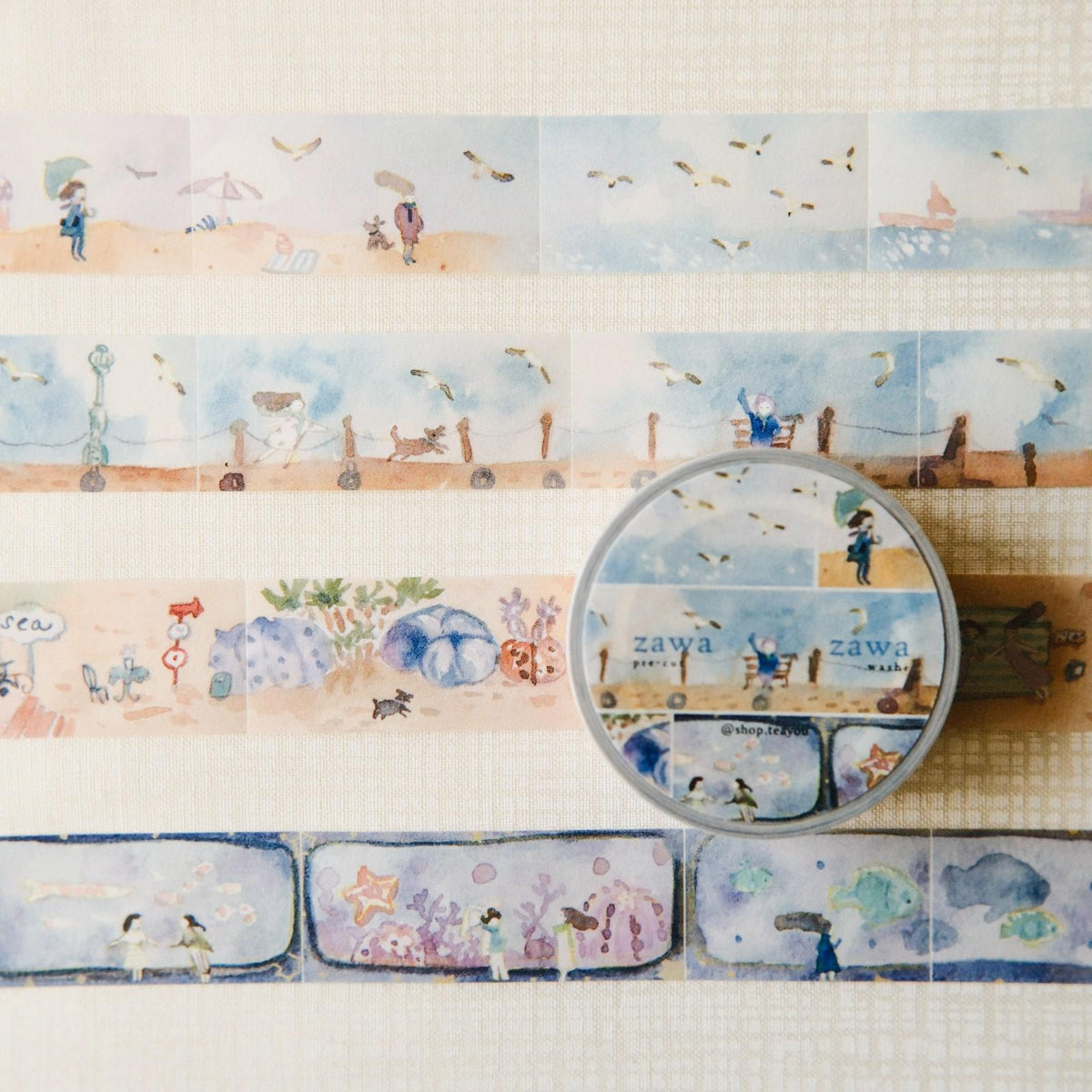 Decorative paper strips with illustrations and a circular container labeled 'zawa' on a textured surface.