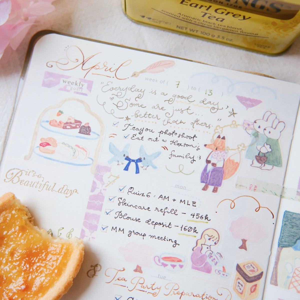 Weekly planner with illustrations and a box of Earl Grey tea on a table.