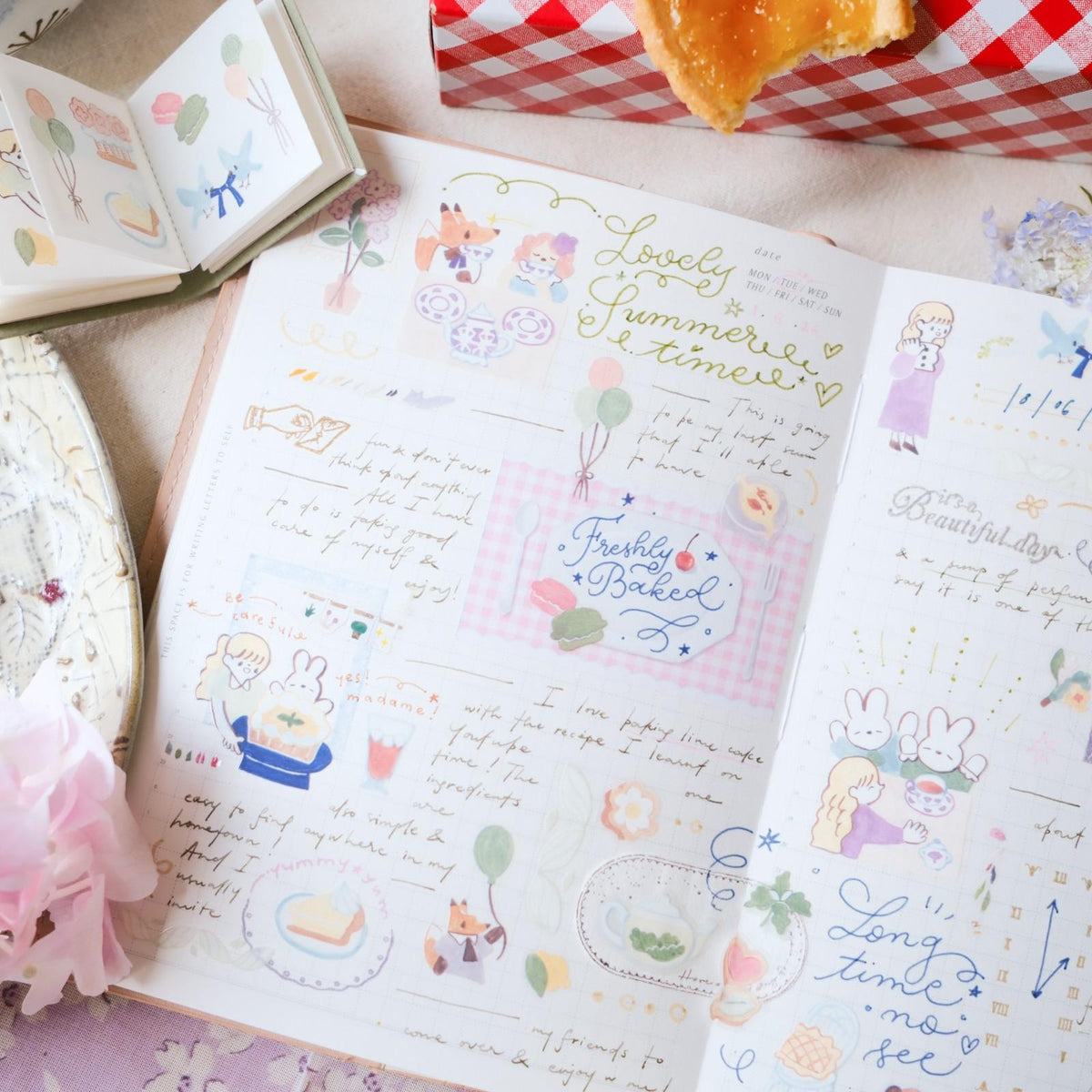 Open book with illustrated pages featuring cute illustrations and text, surrounded by a cake and a box of cookies.
